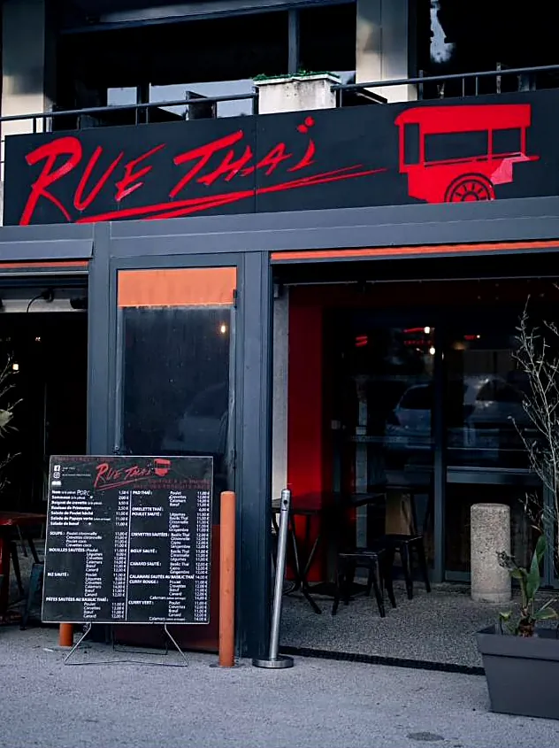 La façade noire de Rue Thaï, enseigne rouge à la charrette et chevalet du menu devant l'entrée.