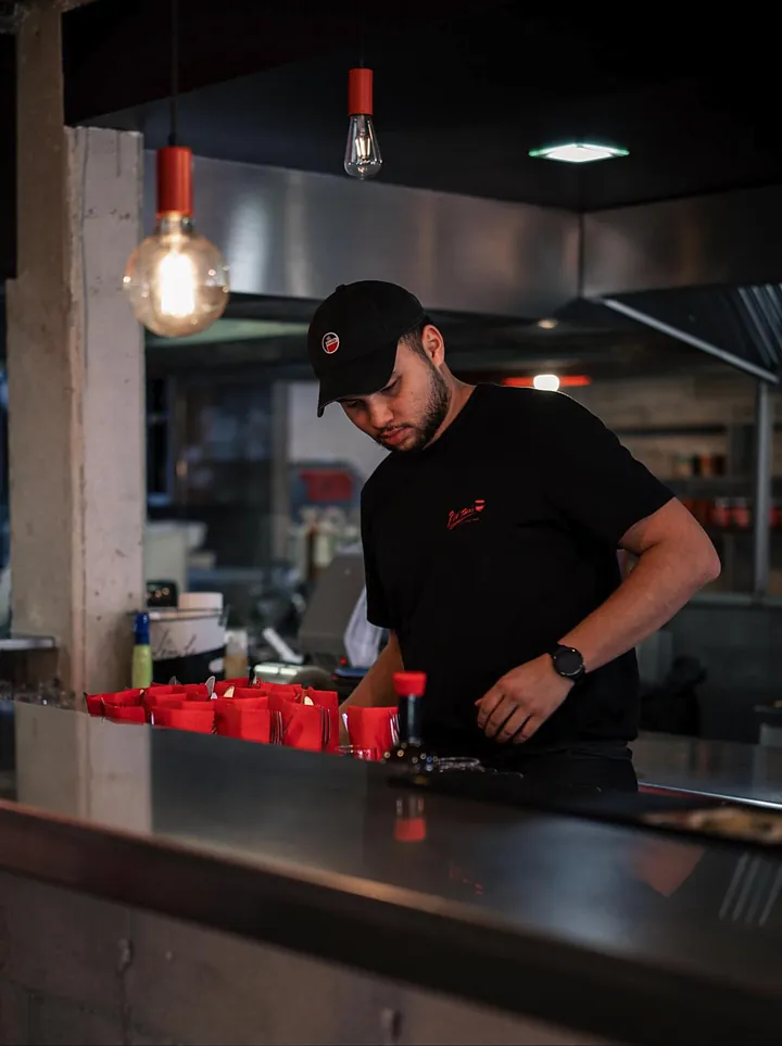 Un membre de l'équipe en casquette et T-shirt au logo, au comptoir, près des serviettes rouges.