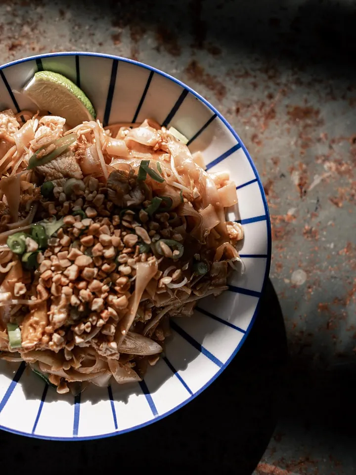Pad thaï aux cacahuètes et au citron vert, dans une assiette à rayures bleues.