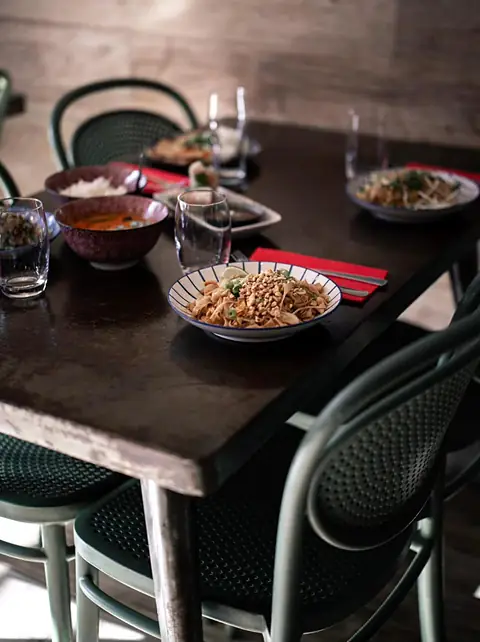 La salle : tables en bois sombre dressées avec des plats, chaises vert sauge.